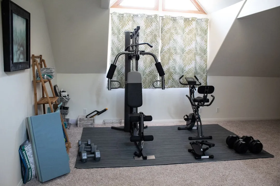 Home gym scene with strength machine, exercise bike, dumbbells, and mats